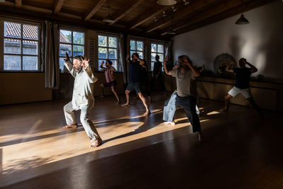 Full body view of mature male instructor demonstrating technique of chi kung exercise for group of people during practice in studio