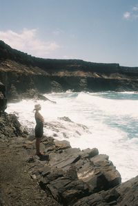 Man standing on rock by sea against sky