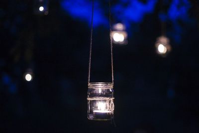 Lit candle in jar hanging at night