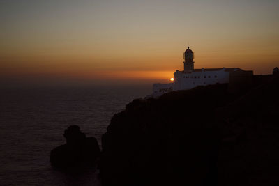 Silhouette buildings by sea against sky during sunset