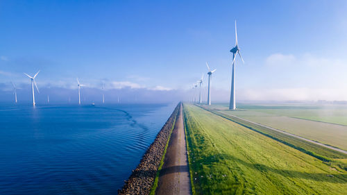 Panoramic view of wind turbines on field against sky