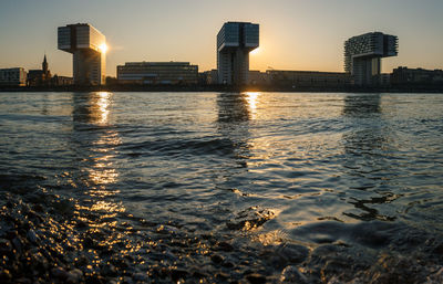 City buildings by sea against sky during sunset