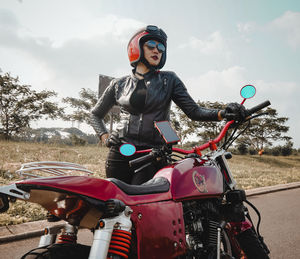 Portrait of woman riding motorcycle on field against sky