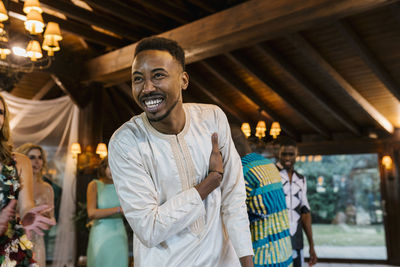 Happy groom dancing while standing with friends in background at banquet