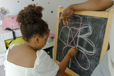 Girl drawing on chalkboard with father standing at home