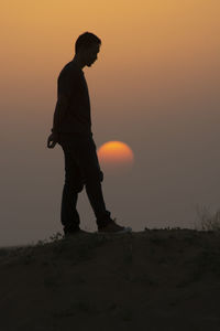 Side view of silhouette man standing on land against sky during sunset