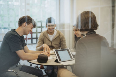 Happy young students studying at table together seen through glass in university