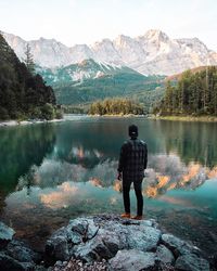 Rear view of man standing by lake against mountains