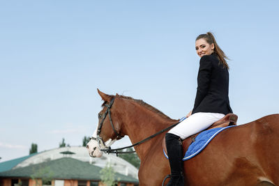 Portrait of young woman with horse standing against clear sky