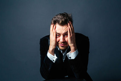 Portrait of young man with head in hands sitting against gray background