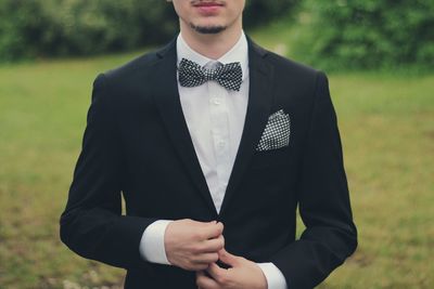 Mid section of young man in bow tie standing on field