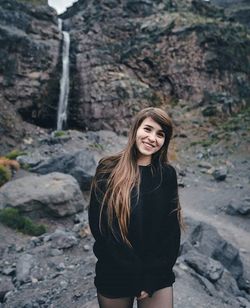 Portrait of smiling woman standing against rocky cliff