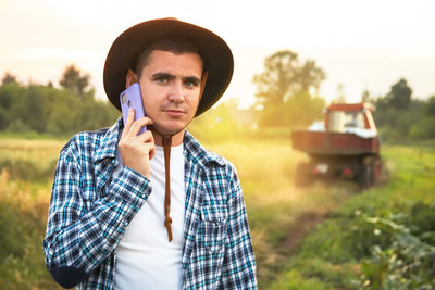 Young farmer talking phone on tractor background. amidst a vast field, a farmer confidently walks