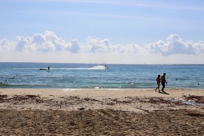 Couple walking on beach against sky during sunny day