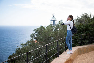 Woman holding camera while standing by railing