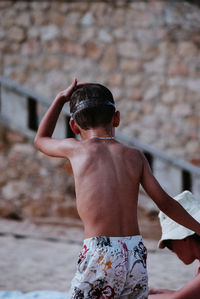 Rear view of shirtless boy standing by mother at beach
