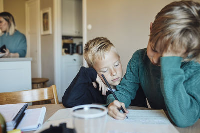 Boy leaning on elbow while looking at brother doing homework