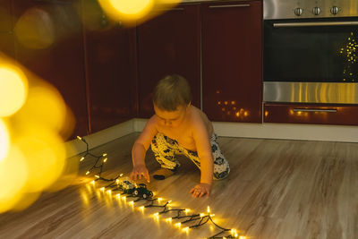 Full length of cute boy sitting by illuminated lights on floor