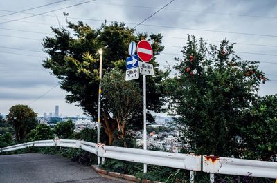 Road sign by trees against sky