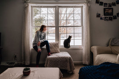 Rear view of girl and her cat looking through window