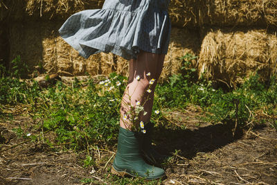 Young girl in rubber boots with flowers standing against the background of straw bales on country 