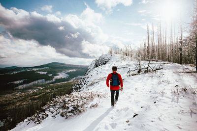 Rear view of man walking on snow against sky during winter