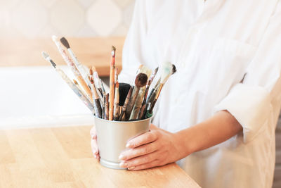 Midsection of woman arranging paintbrushes in jar on table