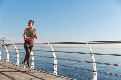 Full length of woman running by railing against sea