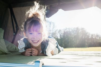 Portrait of a young girl sat in a roof top tent smiling at sunset