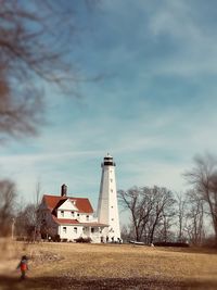 Lighthouse on field by building against sky