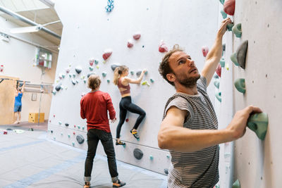 Male and female students practicing wall climbing while mature coach training in gym