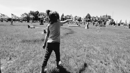 Rear view of girl pointing while walking on grassy field