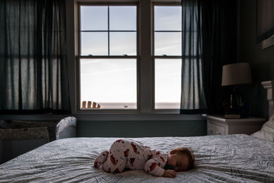 Infant sleeping on bed with view of the ocean outside the window