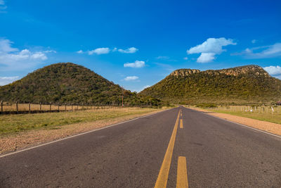 Empty road by mountain against blue sky