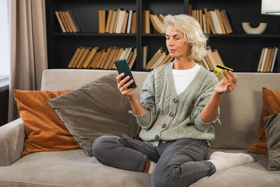 Young woman using phone while sitting on sofa at home