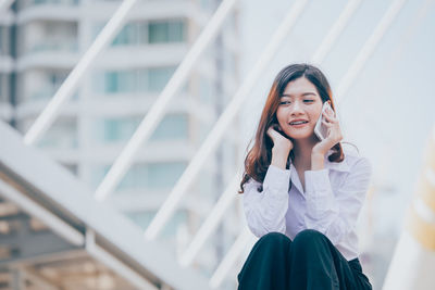 Low angle view of young woman using mobile phone while sitting outdoors