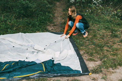 A young woman is resting in the forest, putting up a tent