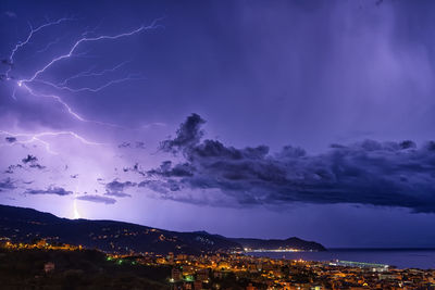 Scenic view of illuminated cityscape against storm clouds at night