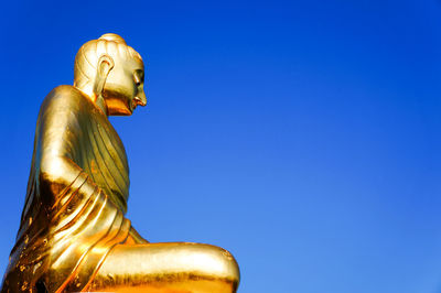 Low angle view of buddha statue against clear blue sky