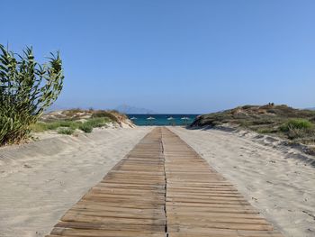 Surface level of footpath by sea against clear blue sky