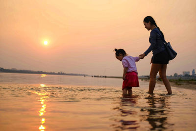 Side view of a couple standing at beach against the orange sky