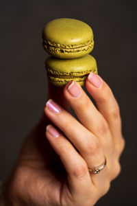 Close-up of woman hand holding macarons over black background