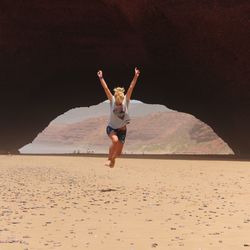 Full length of woman with arms outstretched against rock formation at sandy beach