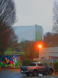 Cars on road by buildings against sky during sunset