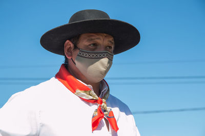 Mature man wearing mask looking away against clear blue sky