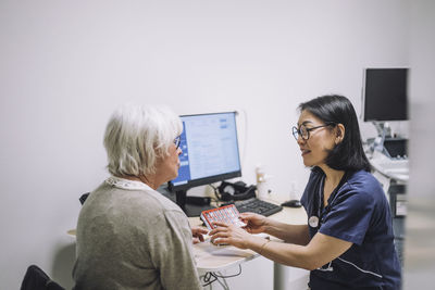 Mature female doctor discussing over pill organizer with senior patient in hospital