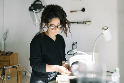 Female artist working with magnifying glass and grinder on jewelry