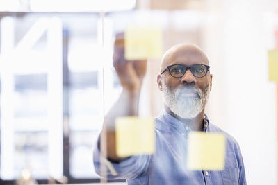 Portrait of businessman taking adhesive note from glass wall in office