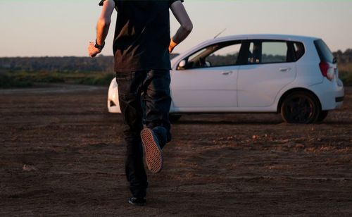 Man running toward a white car on a dirt road