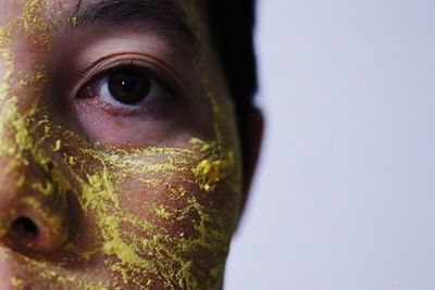 Close-up portrait of woman applying facial mask against wall